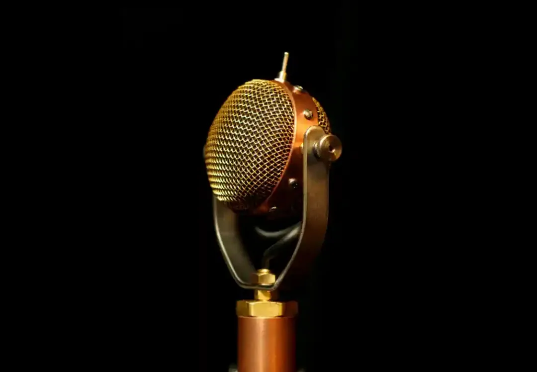 A vintage copper and brass ribbon microphone lit against a black background